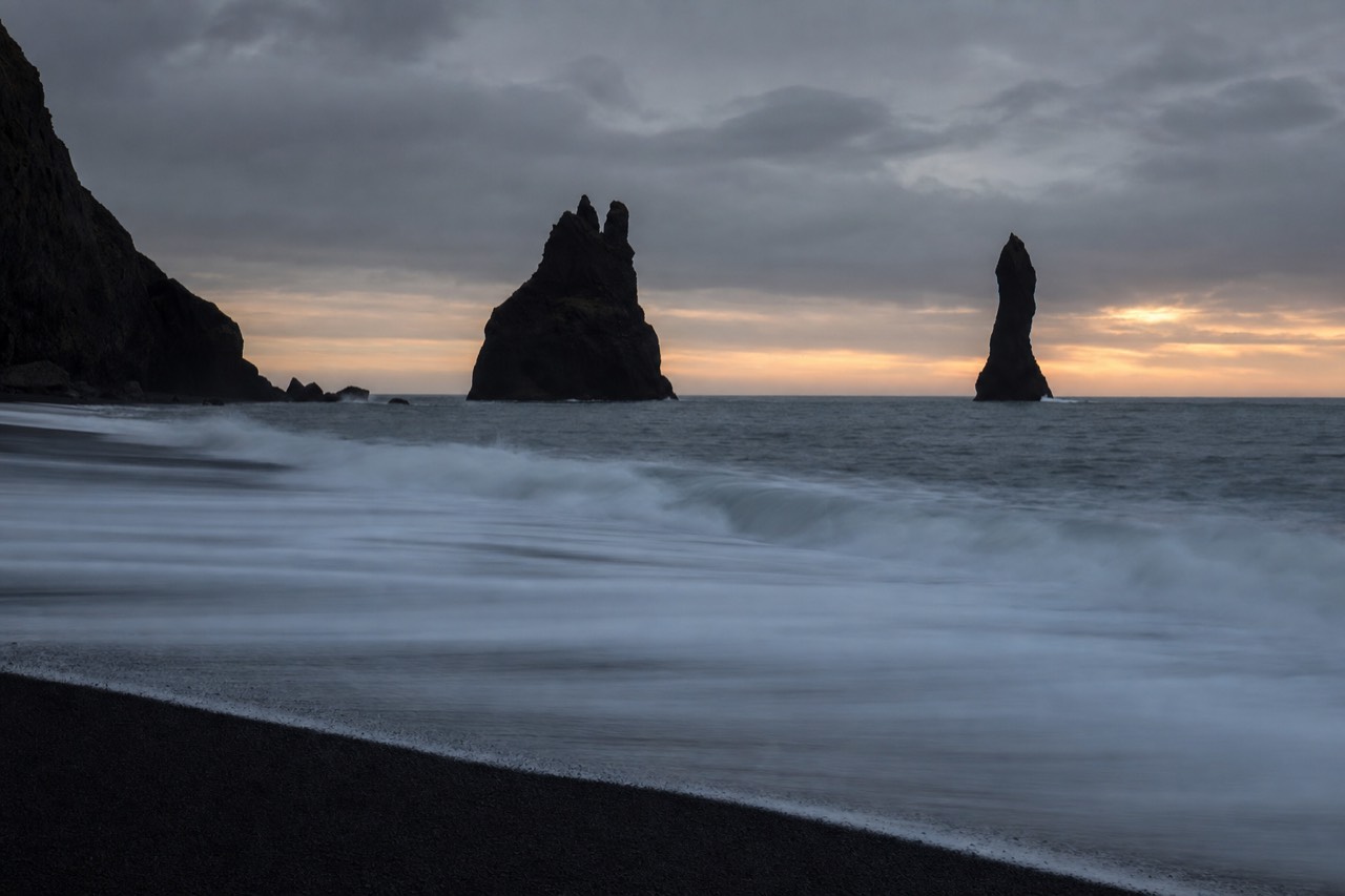 Reynisdrangar sea stacks at dusk, geology unchanged above the shifting sand line