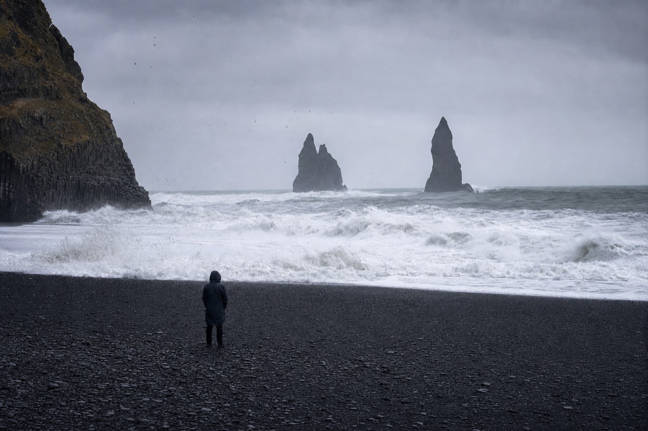 A visitor watching the surf from a safe distance at Reynisfjara