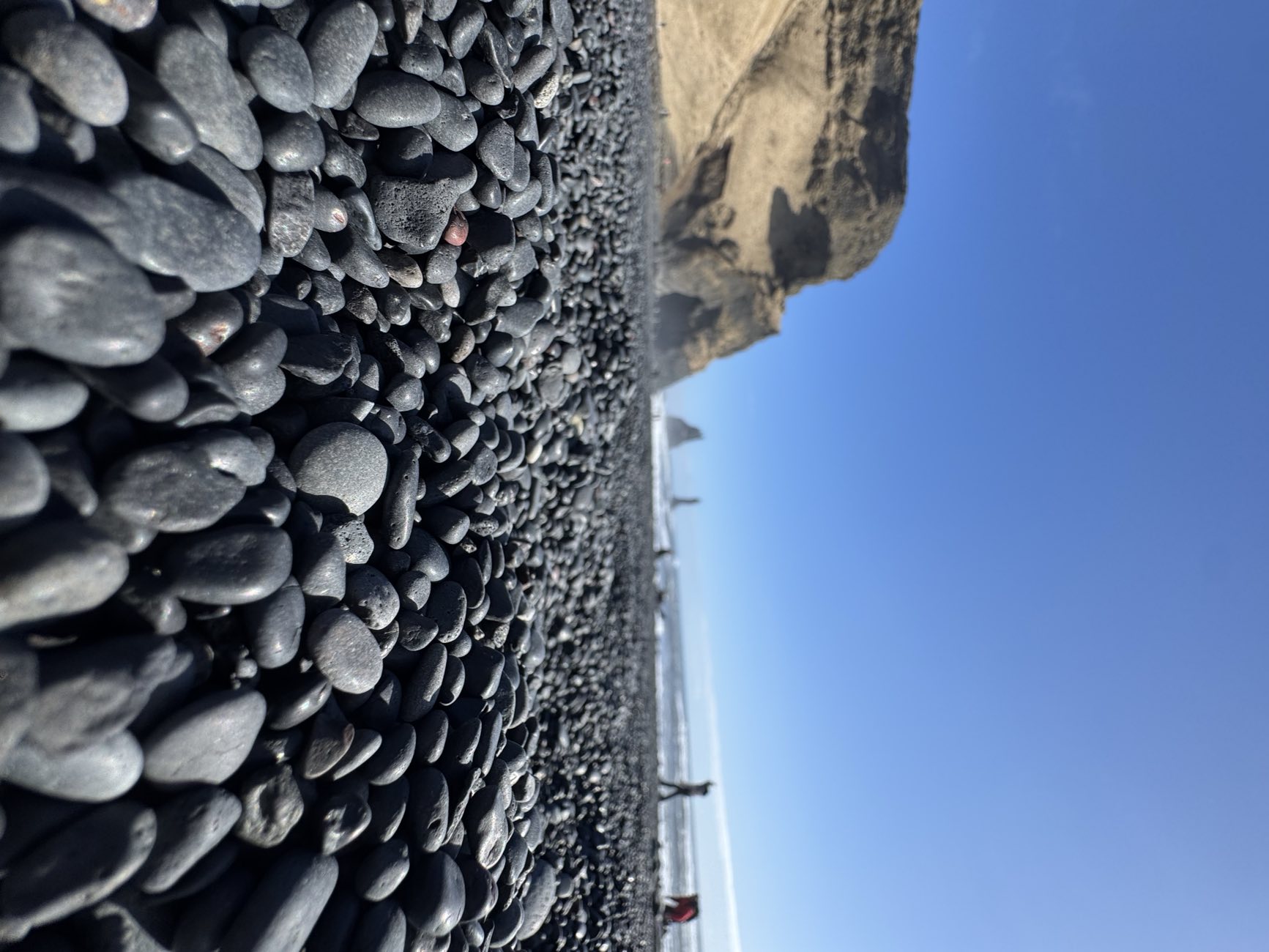 Smooth black basalt pebbles in the foreground with the Reynisfjall cliff and Reynisdrangar sea stacks behind at Reynisfjara