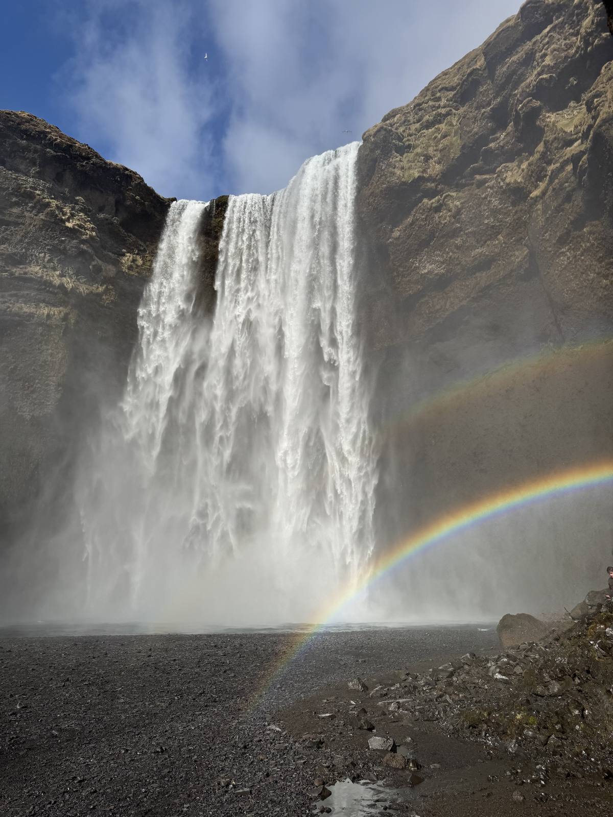 Skogafoss waterfall throwing up spray with a rainbow arcing across its base